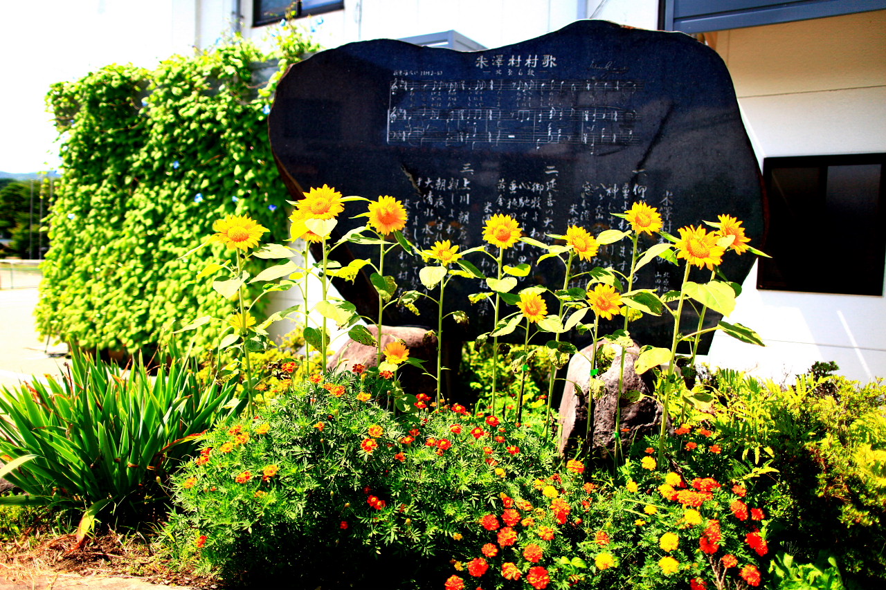 米沢村村歌の歌碑の写真。歌碑の前にはミニヒマワリの花が咲いています。