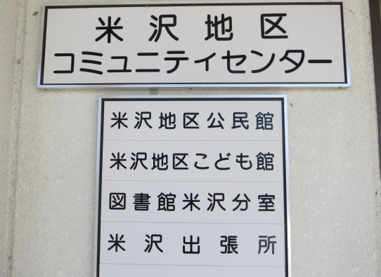 玄関脇にある米沢地区コミュニティセンターの看板の写真。その下には、米沢地区公民館、米沢地区こども館、図書館米沢分室、米沢出張所の看板がついている。