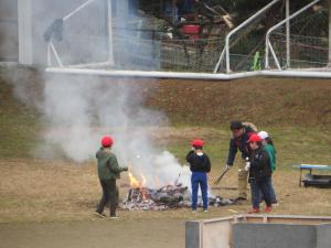 1年生の児童が焚火の周りに集まり火の番をしている様子。