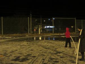 PTA役員の皆さんと支援隊(学校ボランティア)の皆さんが夜の校庭スケートリンクで水まきをしてくださっている様子。