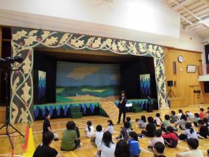 演劇が始まる前に子どもたちが並んで座って、装飾されたステージを見ている様子